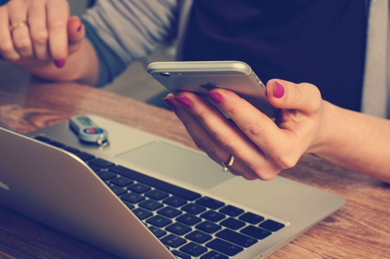 Kobieta trzymająca smartphone i pracująca przy laptopie przy drewnianym stole